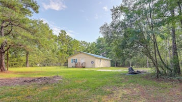 A single-story house with a blue roof, surrounded by a fenced yard and dense trees.