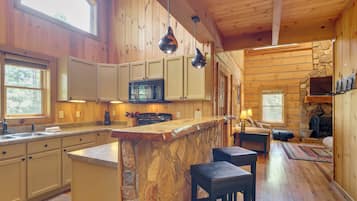 L’intérieur d’une cabane comprend une cuisine, un coin repas et une cheminée en pierre.