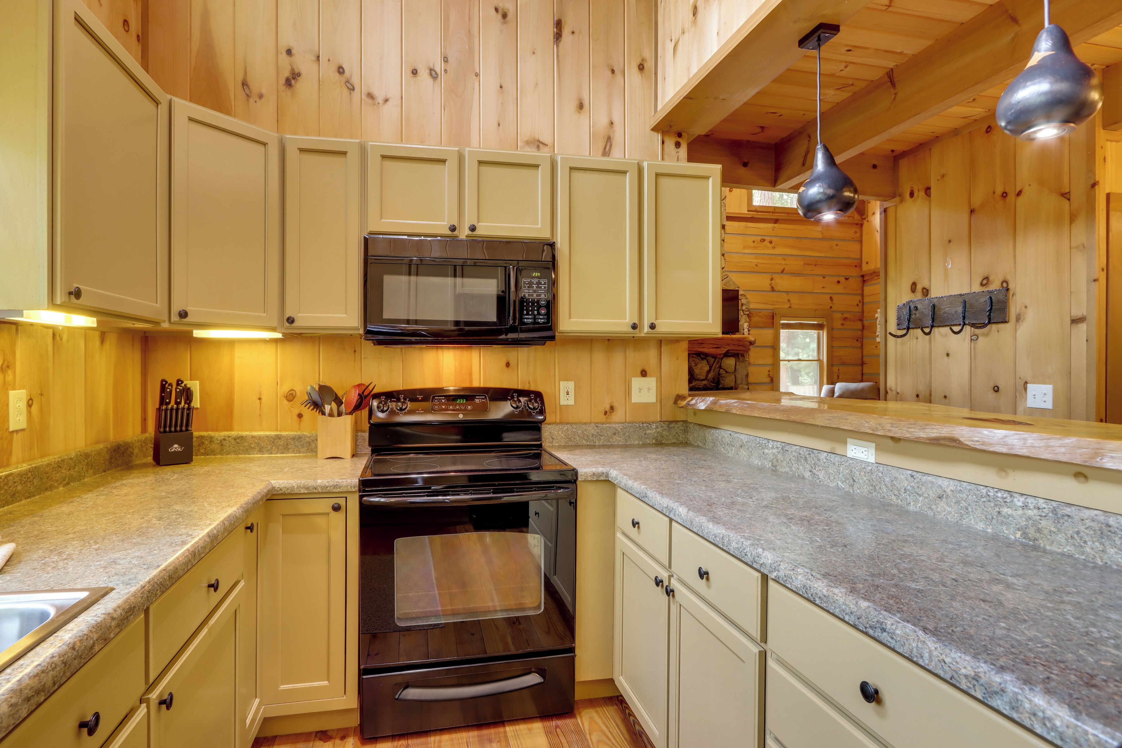 A kitchen with wooden cabinets, a microwave, stove, granite countertops, and hanging pendant lights.