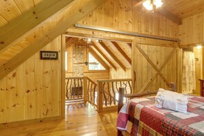 Interior de una cabaña con suelo de madera, una cama con colcha, pared de piedra y un cartel que indica la habitación como 'CABIN'.