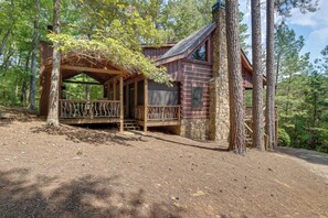 Uma cabana com deck de madeira, paredes de pedra e paisagem florestal natural.