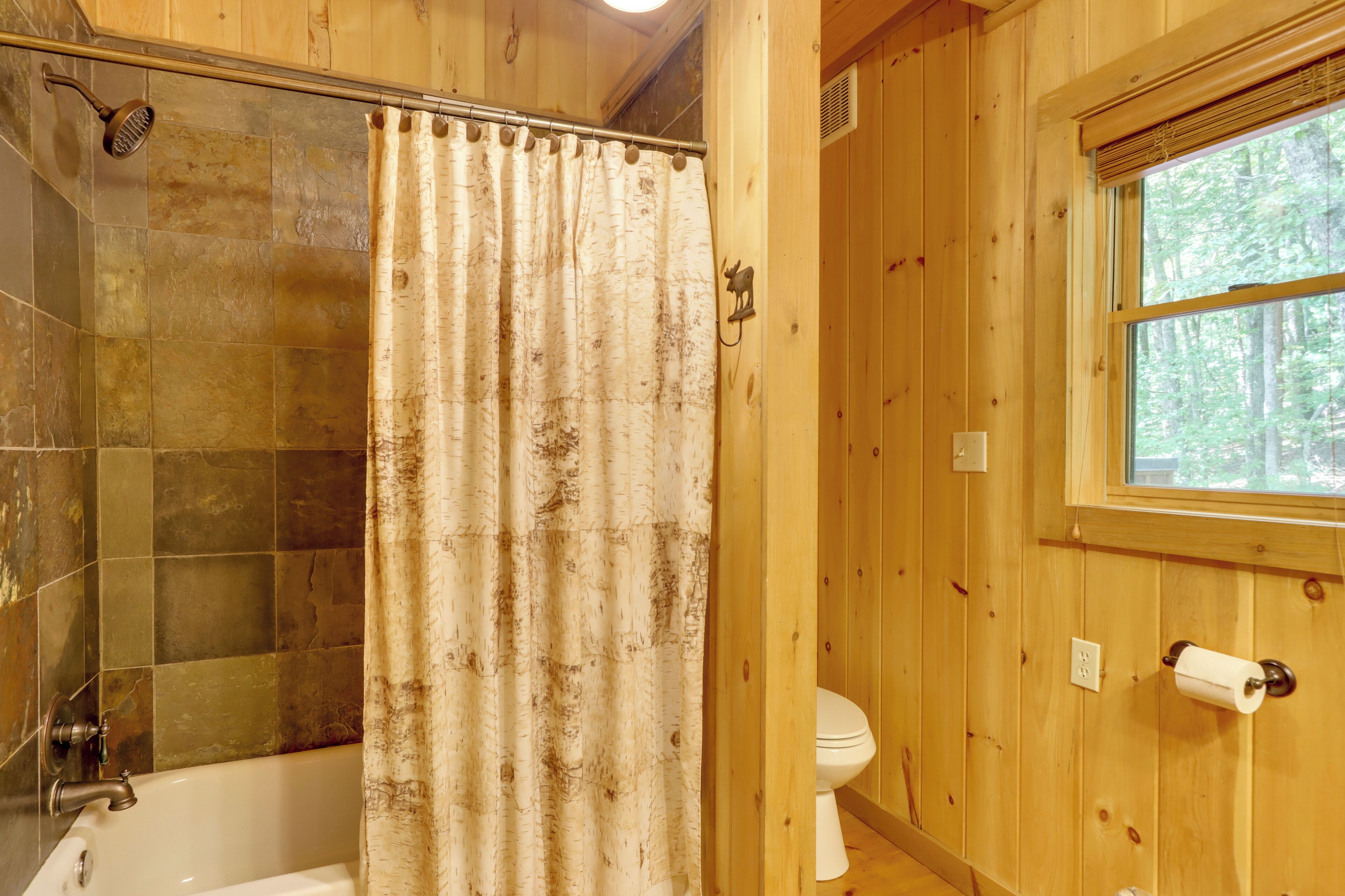 A wooden cabin bathroom with a shower, toilet, and a window.