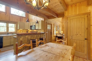 Ein Holzinterieur mit Esstisch, Stühlen, Küchenzeile mit Schränken, einer Steinarbeitsplatte und einer großen Holztür.