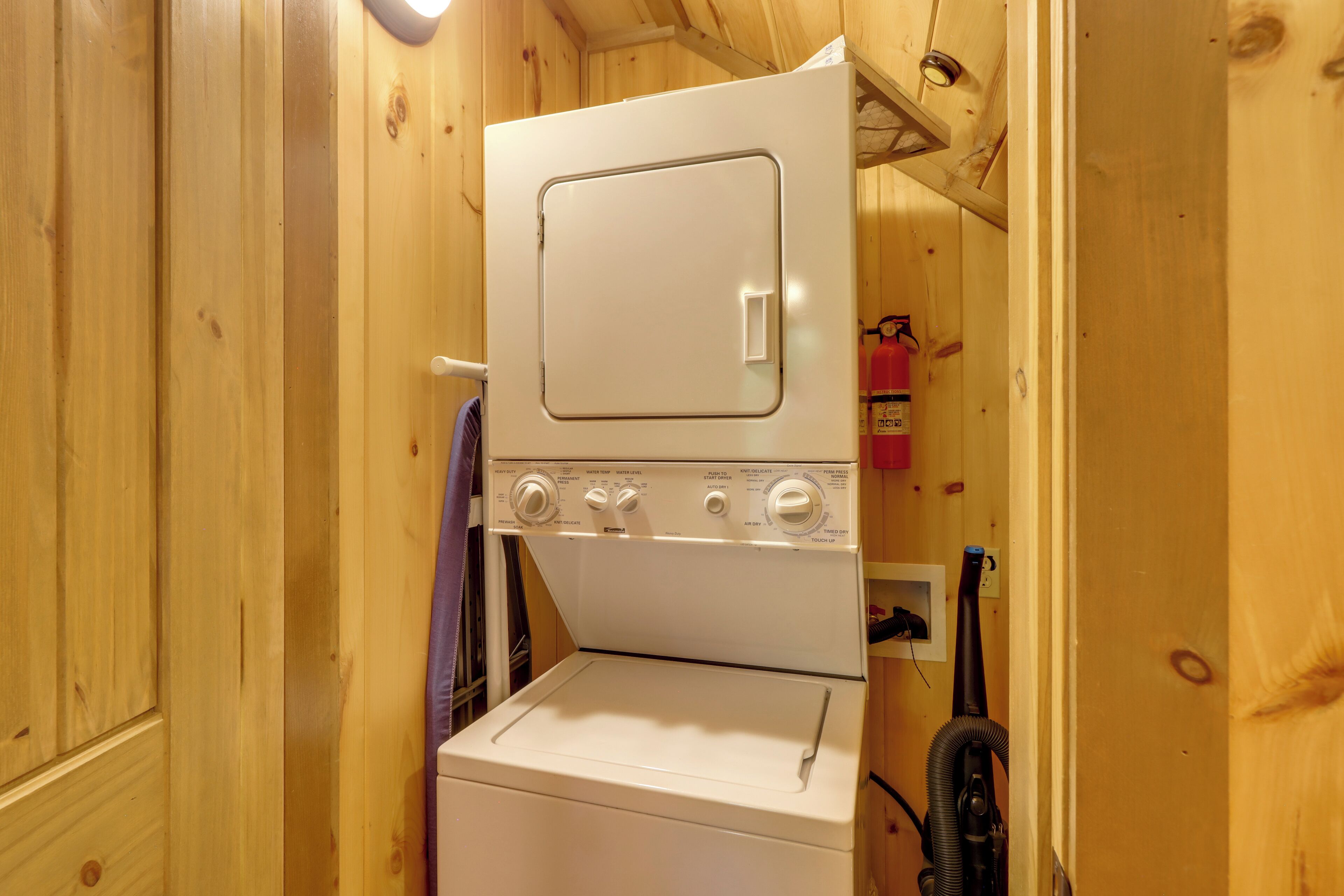 A compact, white, stacked washer and dryer unit in a wooden room.