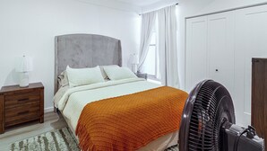 A bedroom with a bed, nightstand, bedside lamp, curtains, and a standing fan. - Colorado River Family Escape in Bullhead City (Bullhead City)