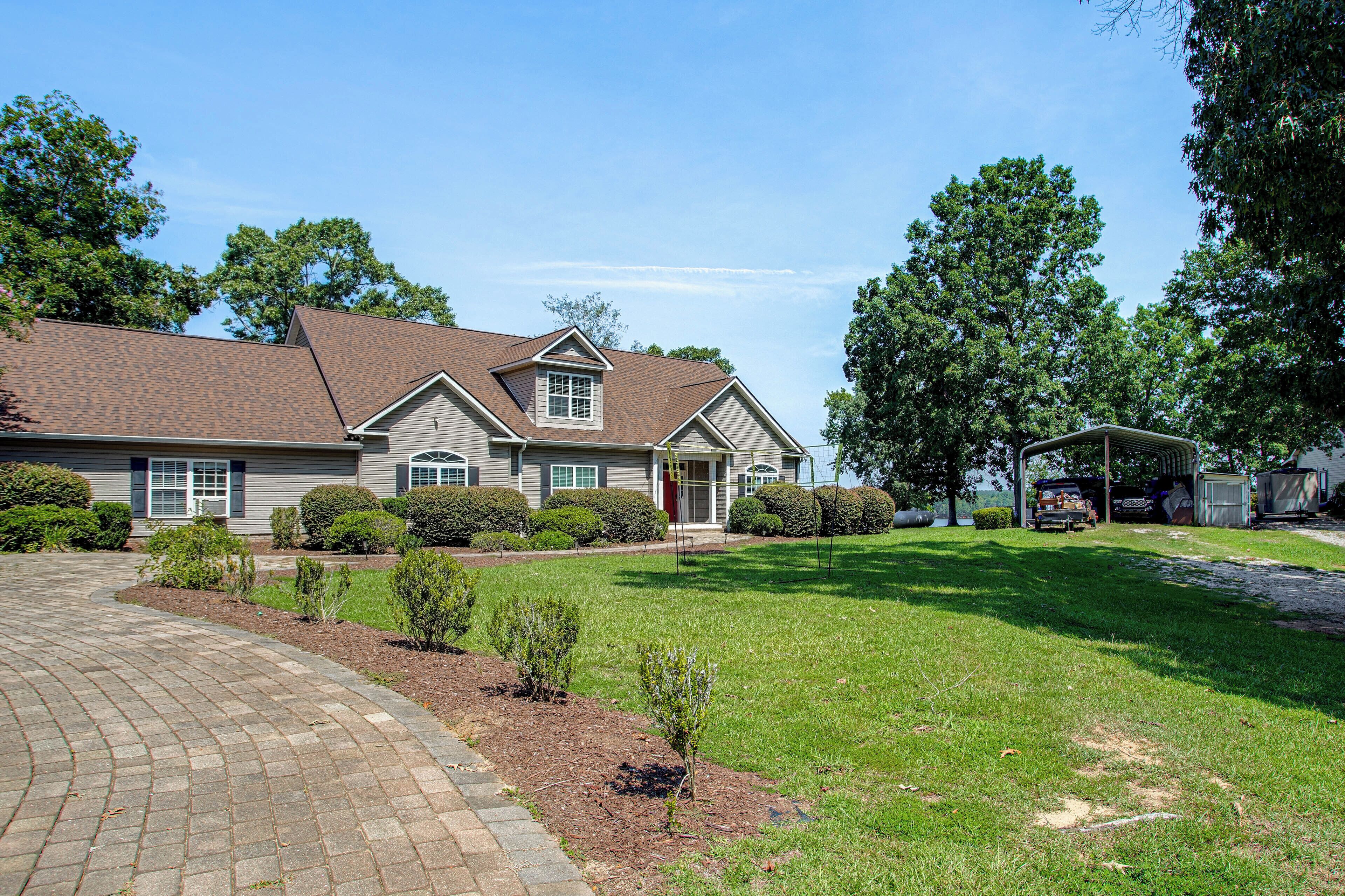 A residential house with a brick driveway, a well-maintained lawn, and a large tree in the background.