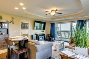 A living room with a sofa, coffee table, and a dining area with a table and chairs. There is a television mounted on the wall and a ceiling fan. - 'the Wake Zone' Condo Near Lake of the Ozarks (Lake Ozark)