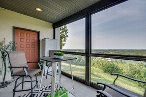 A balcony with a view of a lake and forest, a door, and a table with a plant. - 'the Wake Zone' Condo Near Lake of the Ozarks (Lake Ozark)