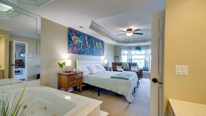 A bedroom with a large bed, a nightstand, a dresser, a ceiling fan, a window with curtains, and a bathroom with a bathtub. - 'the Wake Zone' Condo Near Lake of the Ozarks (Lake Ozark)
