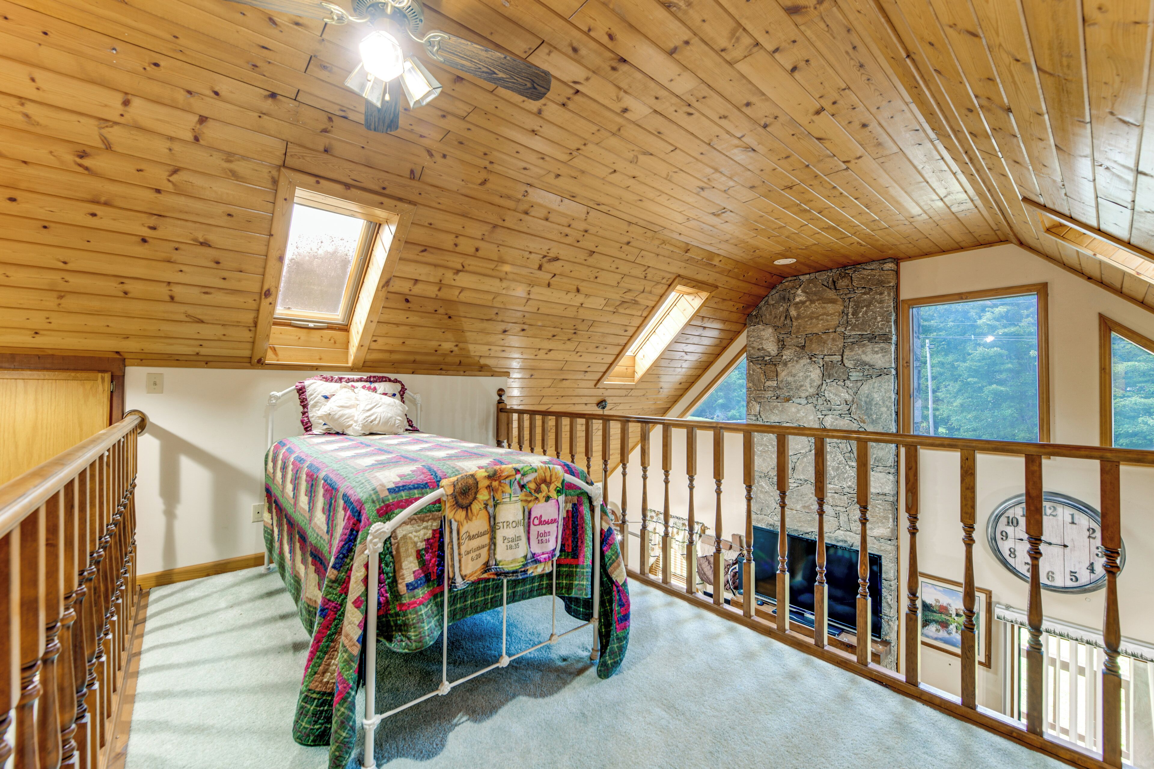 A bedroom with a bed, a window, a clock, and a stone wall.