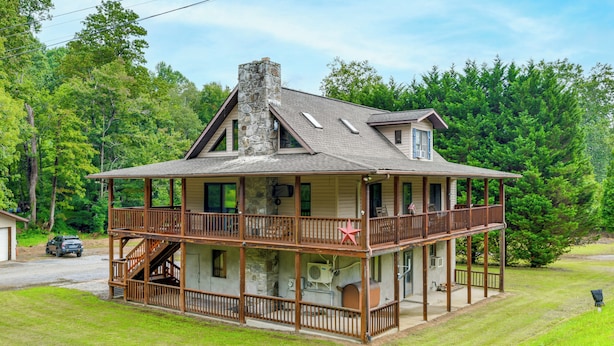 A two-story house with a stone chimney, a covered porch, and a fenced yard. - Creekside Maggie Valley Home w/ Mtn-view Creek-vi (Waynesville)