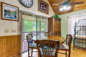 A dining area with a wooden table and chairs, a ceiling fan, and a view through a glass door to the outdoors. - Creekside Maggie Valley Home w/ Mtn-view Creek-vi (Waynesville)