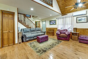 A spacious living room with a wooden staircase, a grey sofa, a purple armchair, and a vintage suitcase. - Creekside Maggie Valley Home w/ Mtn-view Creek-vi (Waynesville)