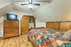 A bedroom with a wooden dresser, a television on top, a ceiling fan, a bed with a colorful quilt, and wooden wardrobes. - Creekside Maggie Valley Home w/ Mtn-view Creek-vi (Waynesville)