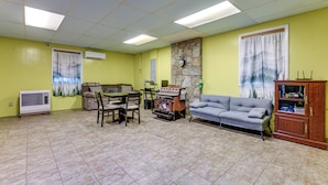 A living room with a stone wall, a fireplace, a sofa, a dining table with chairs, and a kitchen area with a stove. - Creekside Maggie Valley Home w/ Mtn-view Creek-vi (Waynesville)