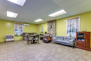 A living room with a stone wall, a fireplace, a sofa, a dining table with chairs, and a kitchen area with a stove. - Creekside Maggie Valley Home w/ Mtn-view Creek-vi (Waynesville)