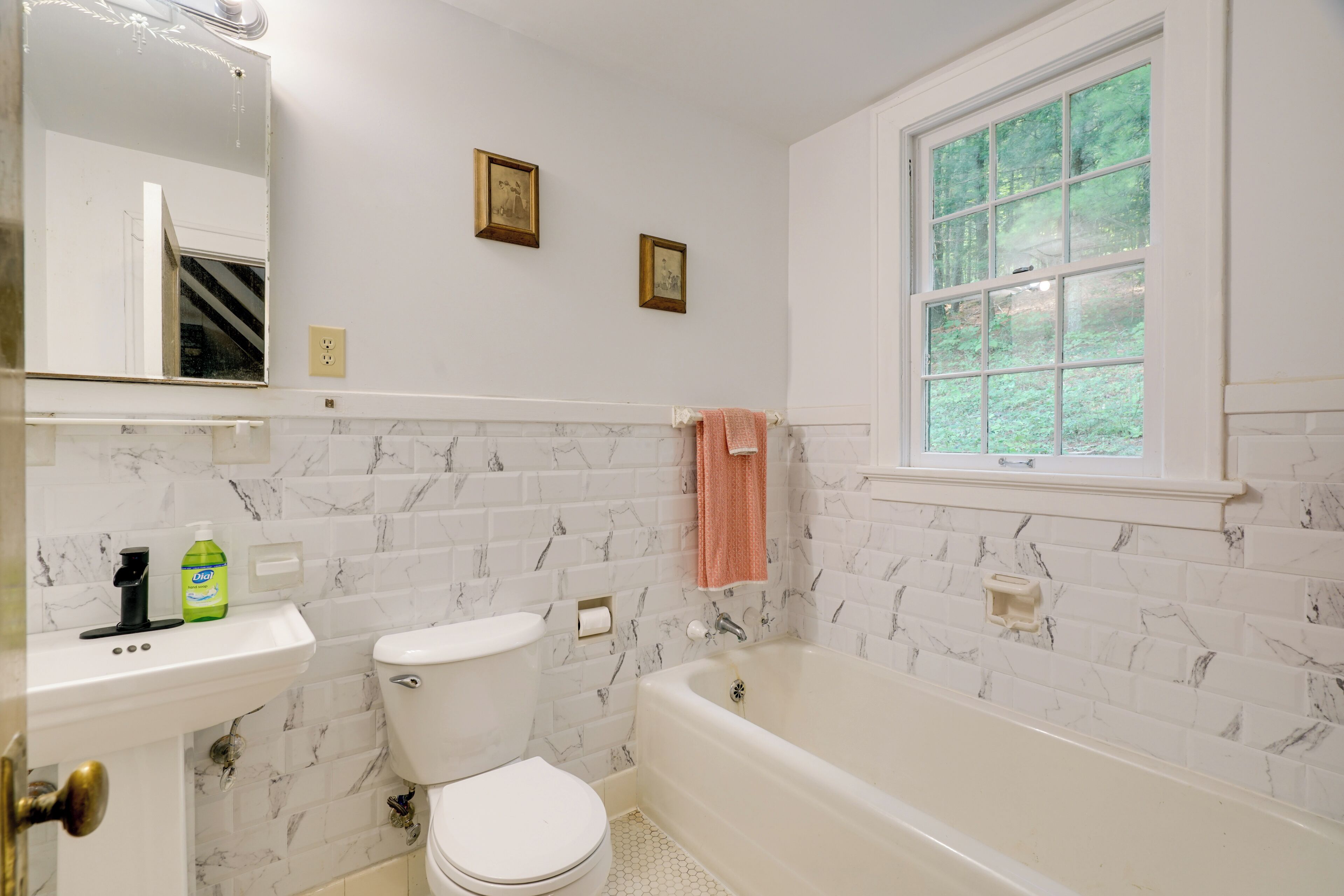 A bathroom with a toilet, sink, and bathtub. There is a window with a view of trees.