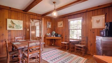 A wooden interior with a dining table, chairs, a kitchen area, and framed artwork on the walls.