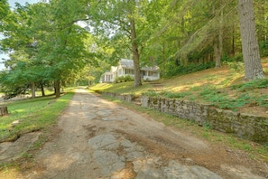 A stone pathway leading to a white house with a porch, surrounded by trees and greenery.