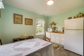 A kitchen with a dining table, chairs, a refrigerator, and a window with a view of greenery.