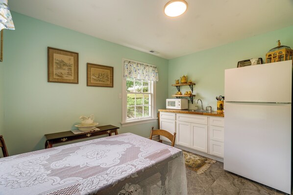 A kitchen with a dining table, chairs, a refrigerator, and a window with a view of greenery.