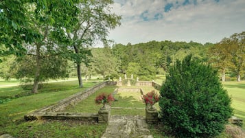 A landscaped garden with stone pathways, a central fountain, and a variety of trees.