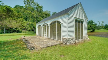 A small, single-story building with a gabled roof and large windows, surrounded by grass and trees.