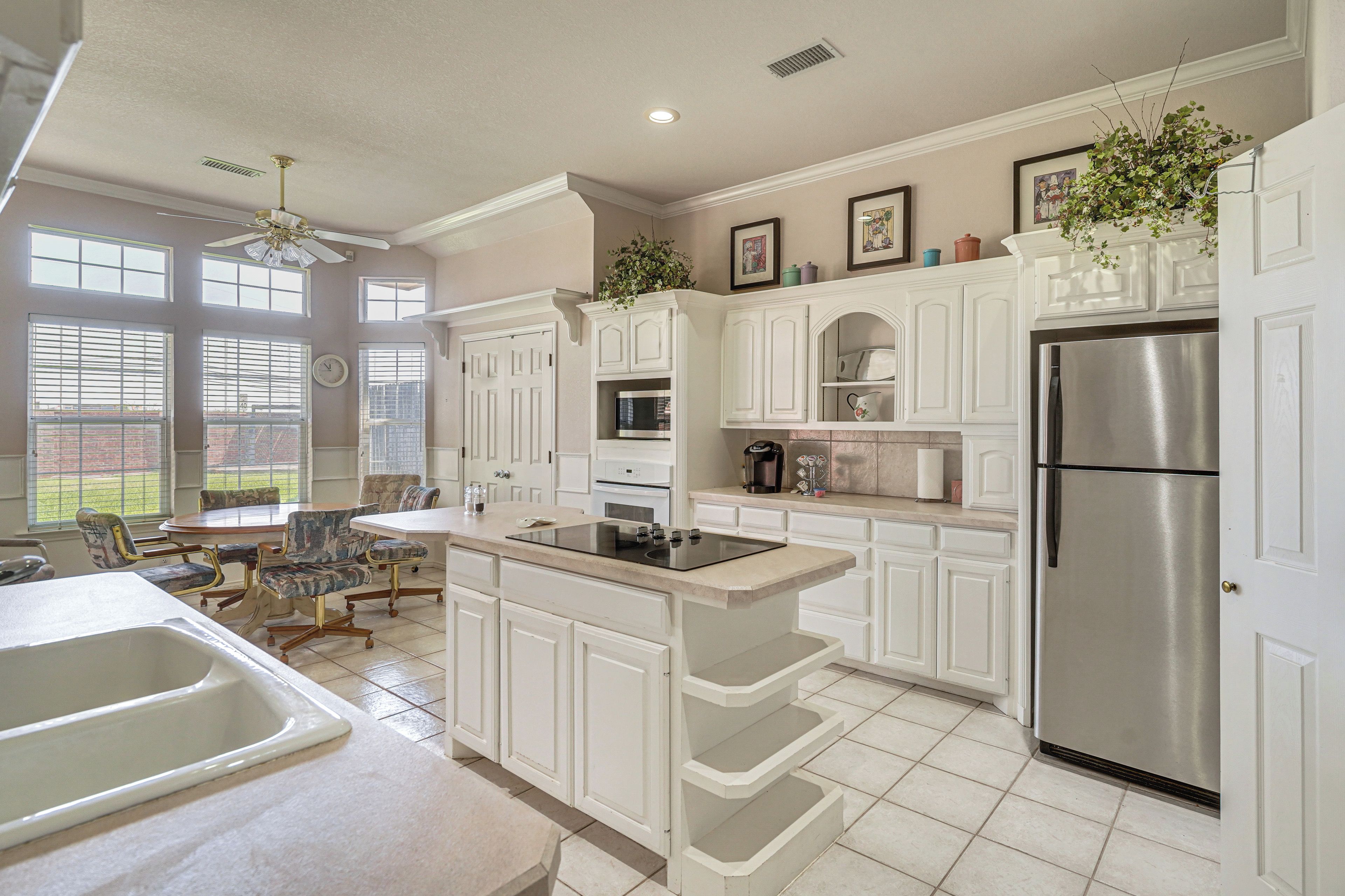 A modern kitchen with white cabinetry, a stainless steel refrigerator, and a dining area with a table and chairs.