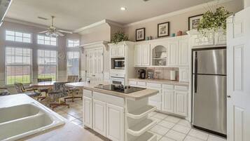 A modern kitchen with white cabinetry, a stainless steel refrigerator, and a dining area with a table and chairs.
