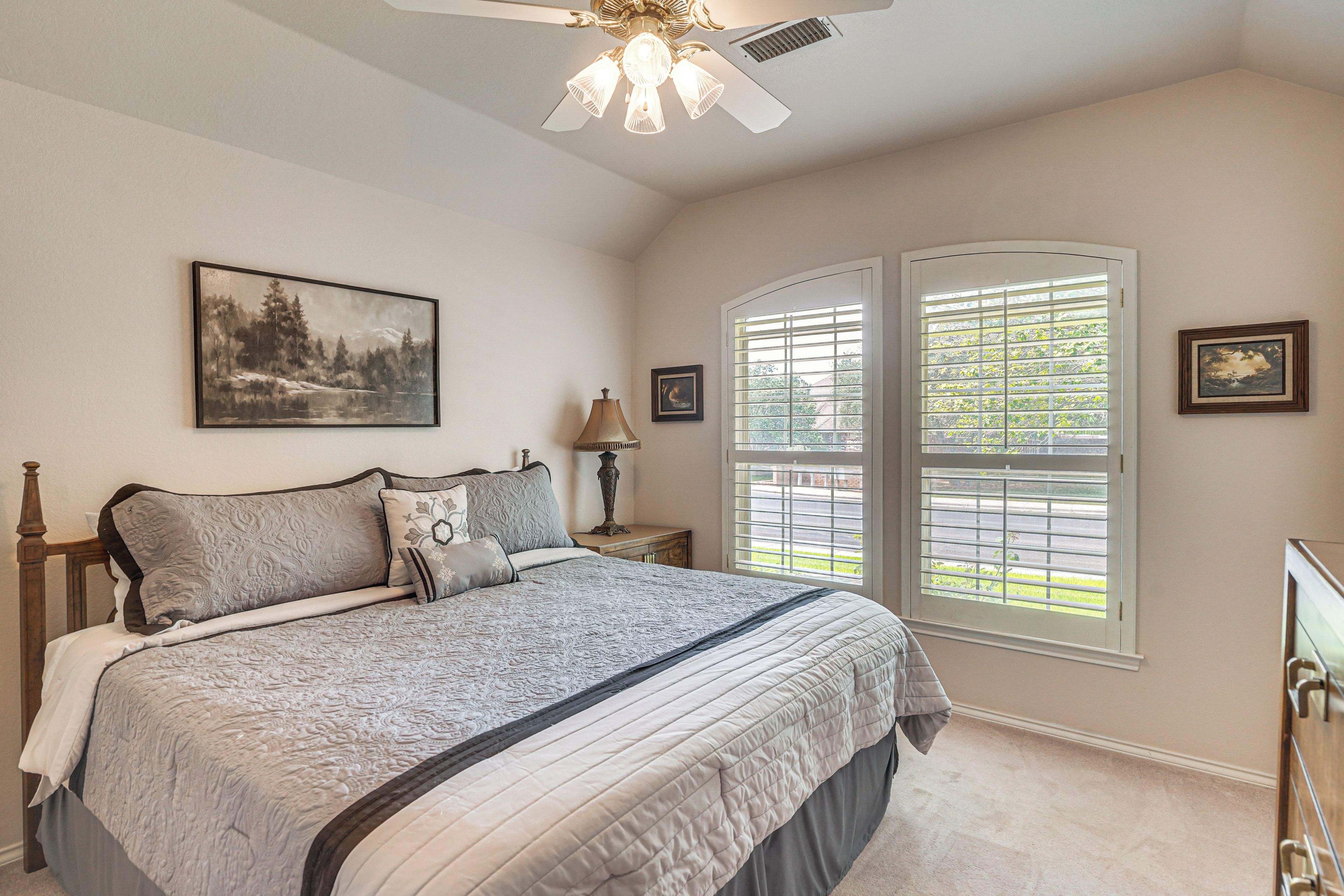A bedroom with a bed, a ceiling fan, a window with blinds, and a painting on the wall.