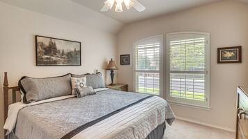 A bedroom with a bed, a ceiling fan, a window with blinds, and a painting on the wall.