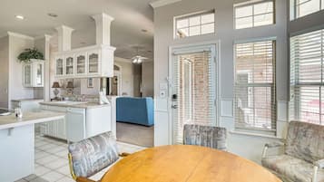 A modern kitchen with white cabinetry, a dining area with a round wooden table, and a living room with a blue sofa.