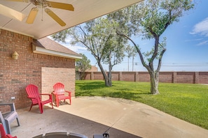 A covered patio area with a brick wall, two red chairs, and a concrete floor. - Spacious Backyard & Patio! Family Haven in Odessa (Odessa)