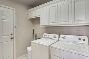 Une buanderie équipée d’un lave-linge et d’un sèche-linge à chargement frontal, d’une porte à serrure et d’un balai appuyé contre le mur.
