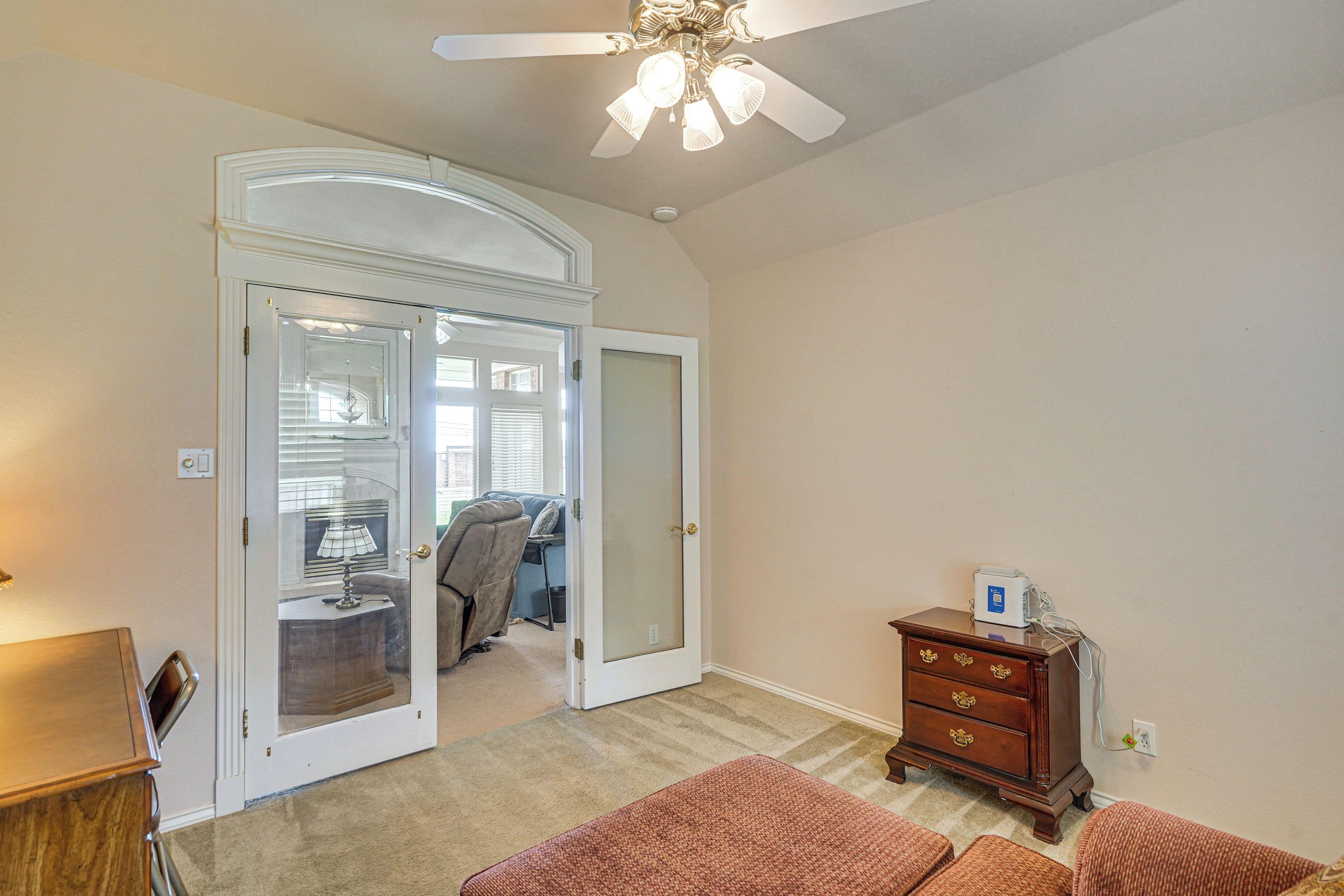 A room with a ceiling fan, a wooden dresser, a door leading to another room, and a carpeted floor.