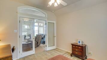 A room with a ceiling fan, a wooden dresser, a door leading to another room, and a carpeted floor.