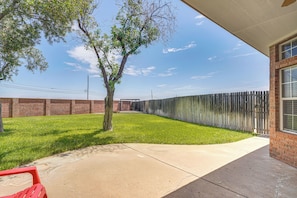 Un jardin avec un arbre, un mur en briques, une clôture en bois et une terrasse en béton.