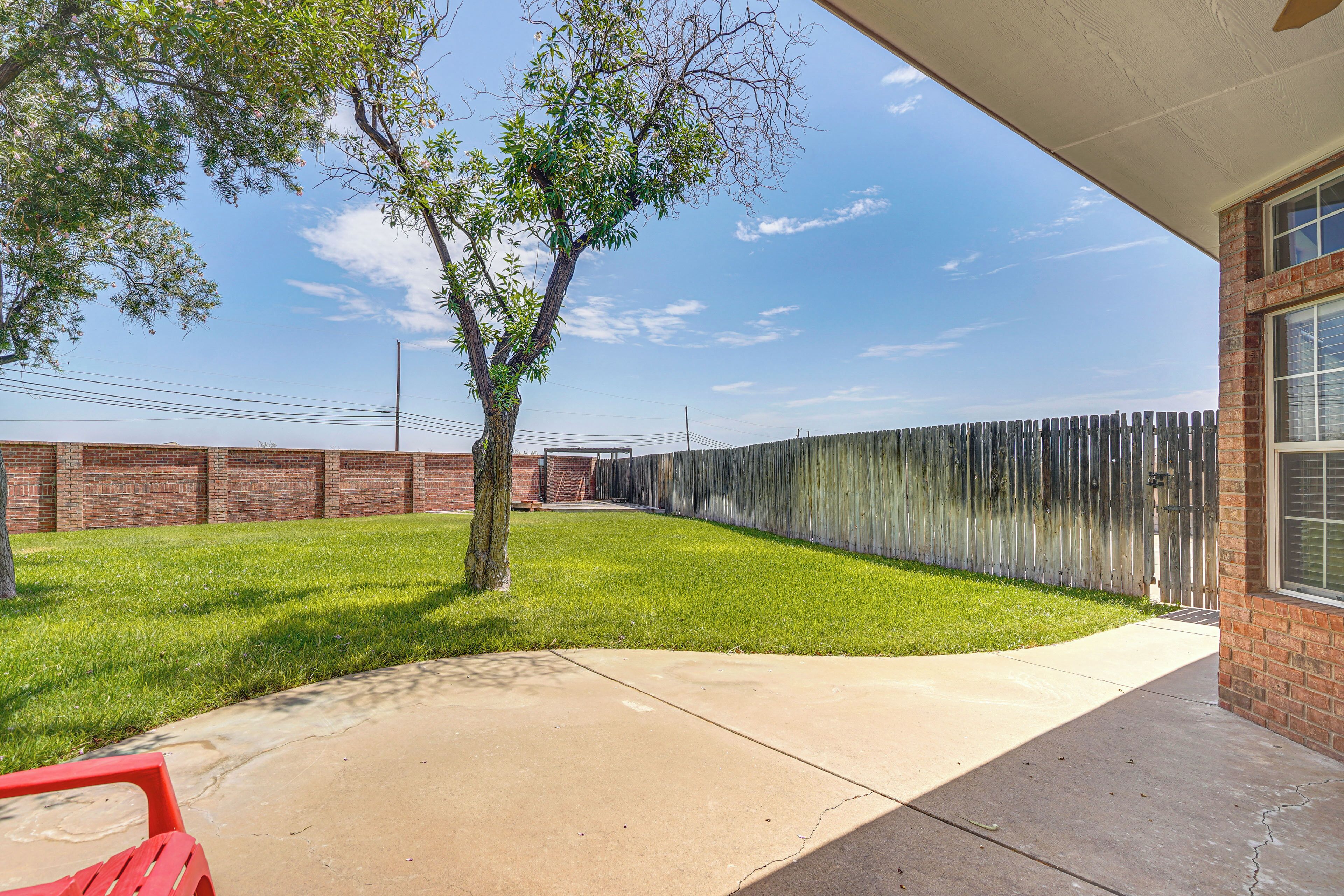 Un patio trasero con un árbol, un muro de ladrillo, una valla de madera y un patio de concreto.