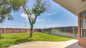 A backyard with a tree, a brick wall, a wooden fence, and a concrete patio.