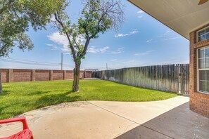 A backyard with a tree, a brick wall, a wooden fence, and a concrete patio.