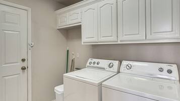 A laundry room with a front-loading washer and dryer, a door with a key lock, and a mop leaning against the wall.