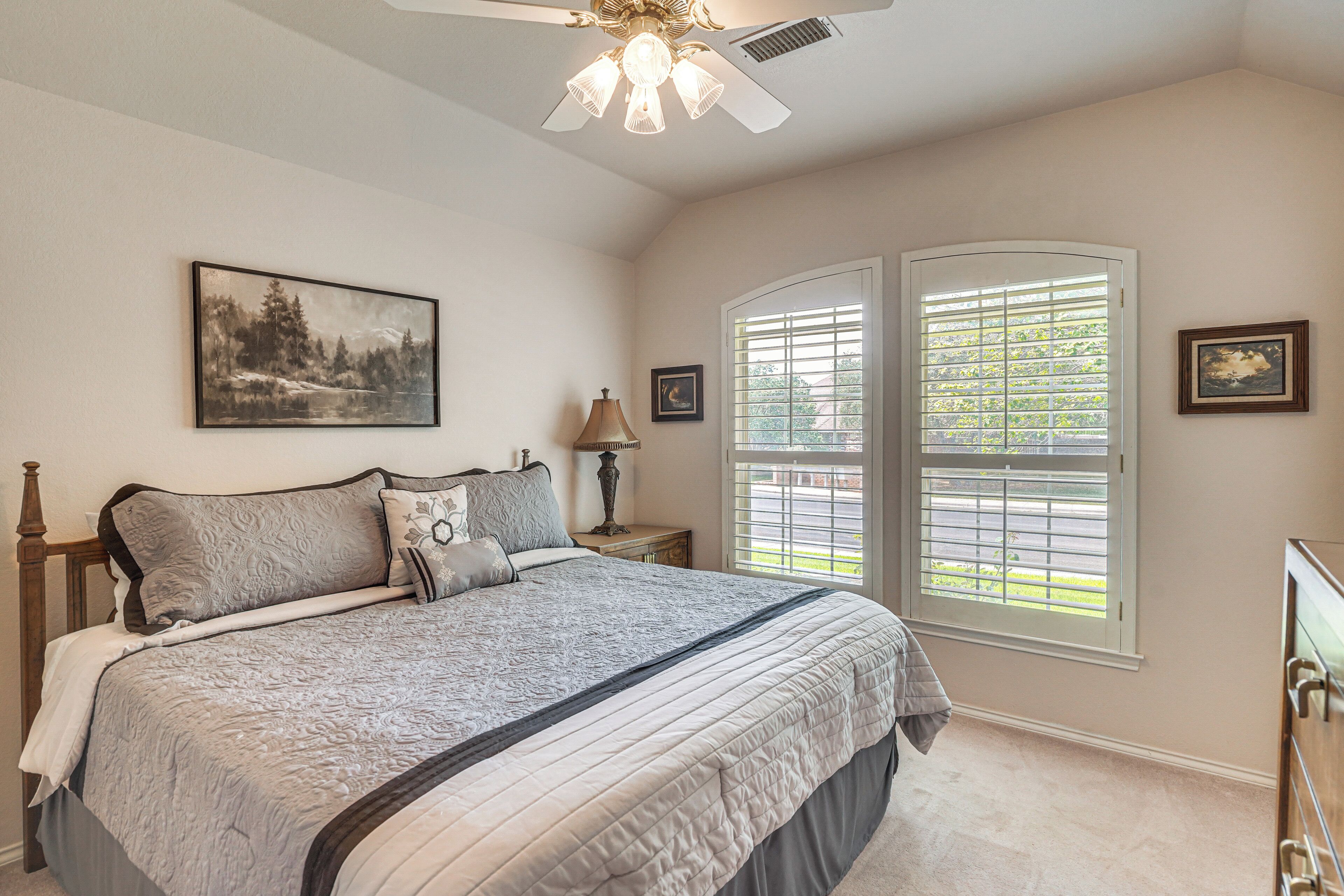 A bedroom with a bed, a ceiling fan, a window with blinds, and a painting on the wall.