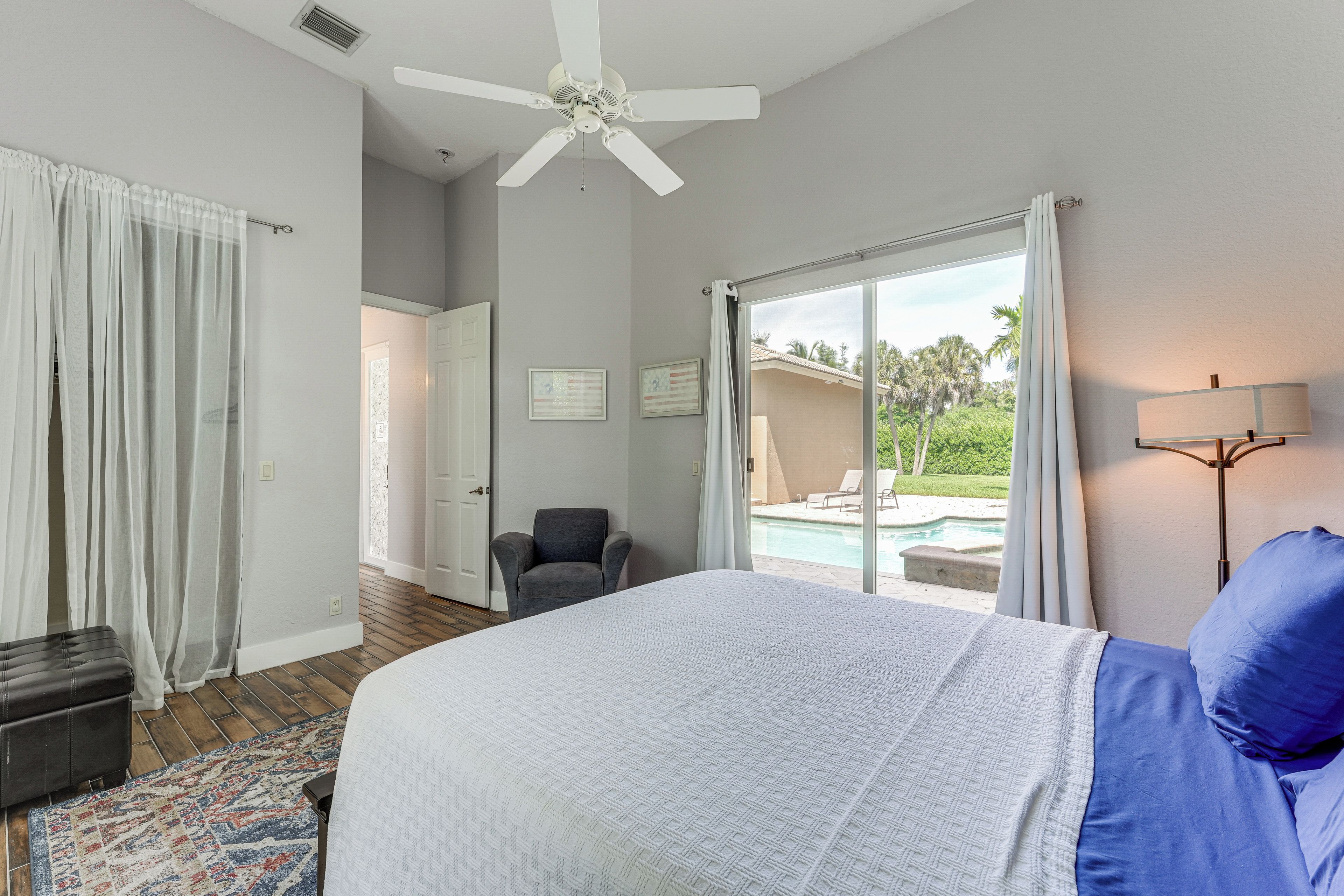 A bedroom with a bed, a chair, a ceiling fan, and a view of a swimming pool.