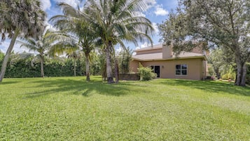 A residential property with a well-maintained lawn, palm trees, and a single-story house with a tiled roof.