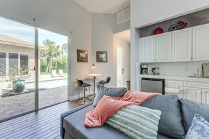 Ein modernes Wohnzimmer mit grauem Sofa, einem Couchtisch und Blick auf einen Pool und Palmen draußen.