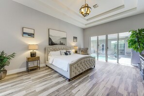 Un dormitorio con una cama grande, dos lámparas de noche, un cuadro enmarcado en la pared y vistas al exterior a través de un ventanal.