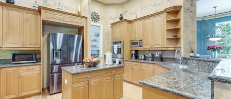 Una cocina con armarios de madera, electrodomésticos de acero inoxidable, encimeras de granito y vista a un jardín por la ventana.