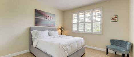 A bedroom with a bed, a chair, a window with blinds, and a painting on the wall.