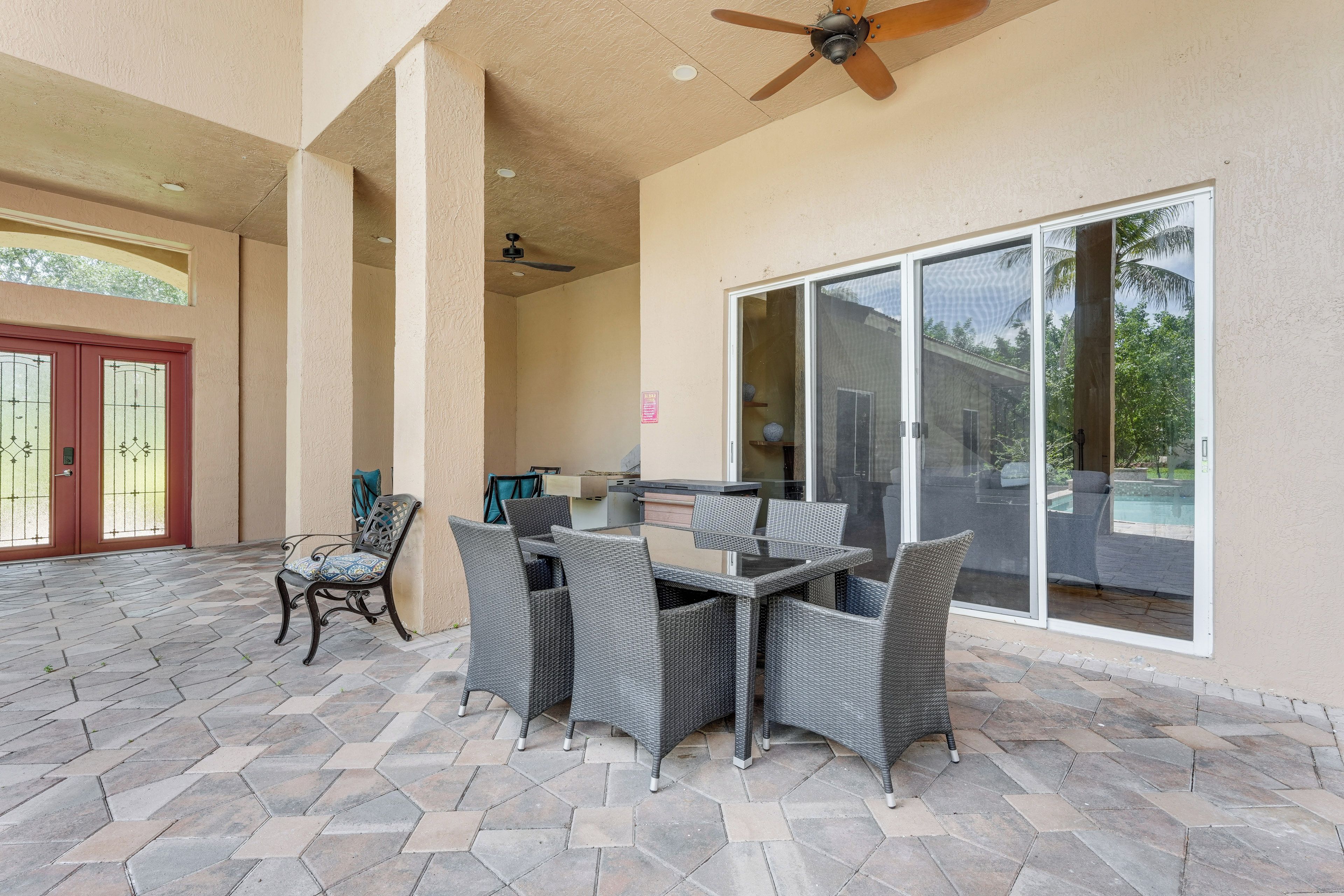 A covered patio area with a dining table and chairs, a ceiling fan, and a sliding glass door leading to a pool.