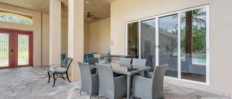A covered patio area with a dining table and chairs, a ceiling fan, and a sliding glass door leading to a pool.
